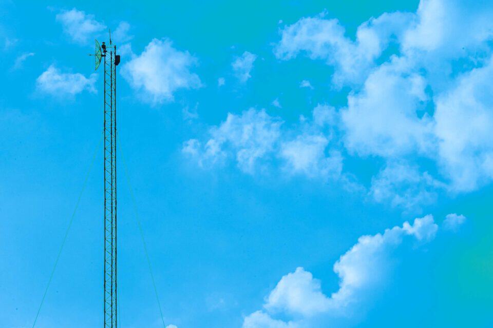 Tall telecommunications mast rising into a bright cloudy sky