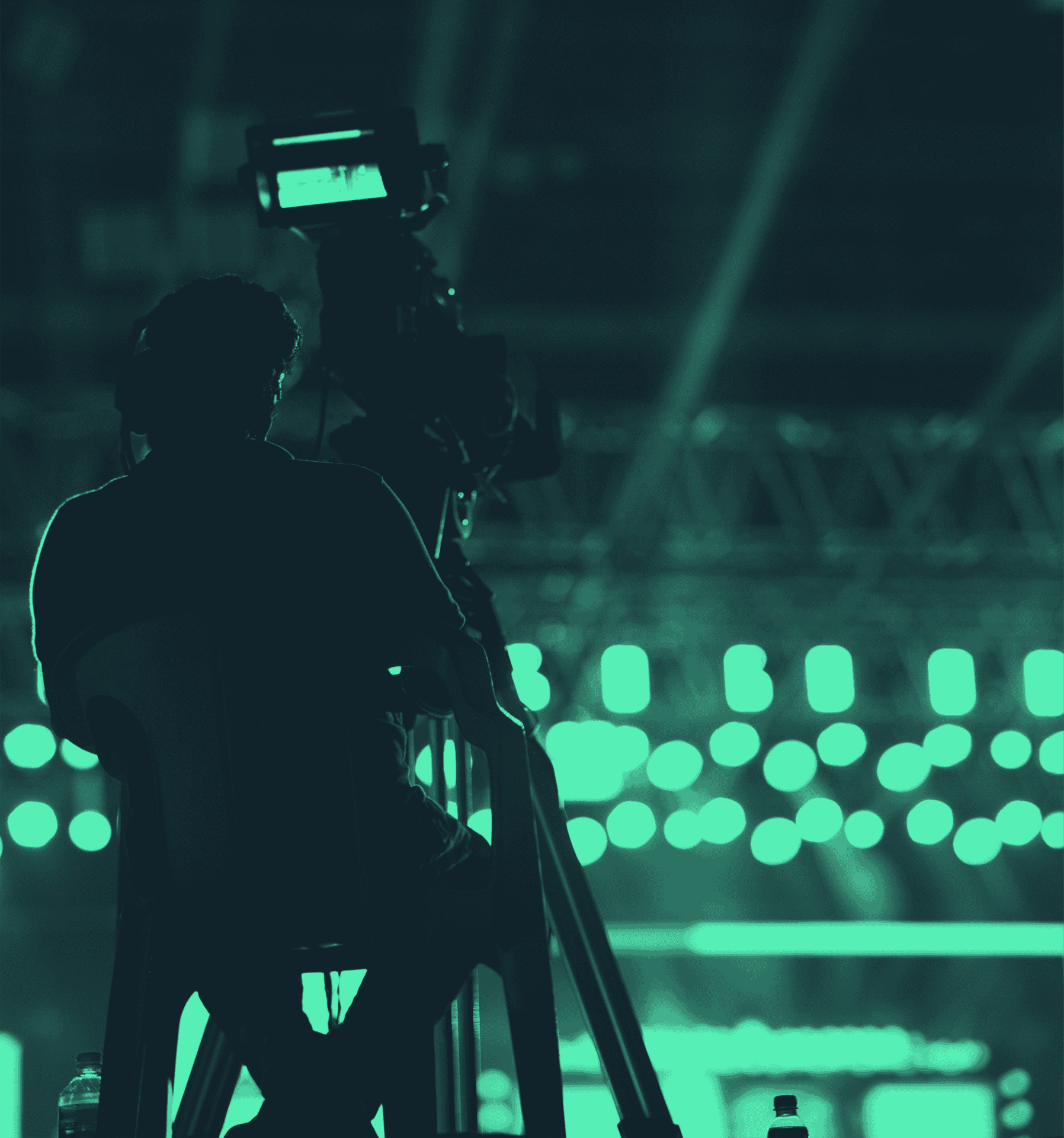 Camera operator filming a live sporting event under green stadium lighting