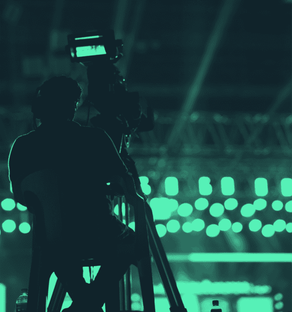 Camera operator filming a live sporting event under green stadium lighting