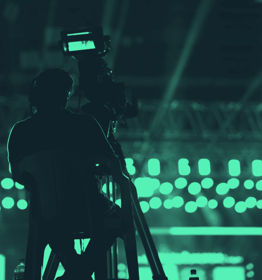 Camera operator filming a live sporting event under green stadium lighting
